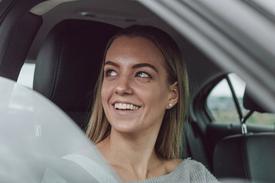 Young woman sitting in car smiling | Auto Insurance